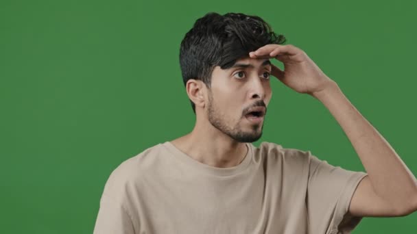 Verwirrt nervösen Kerl arabische hispanische Mann posiert auf grünem Hintergrund legte Kopf an Stirn Blick in die Ferne Spion auf der Suche nach jemandem gucken aus Warten Make Wahl hat schlechte Sehkraft Kurzsichtigkeit - Filmmaterial, Video