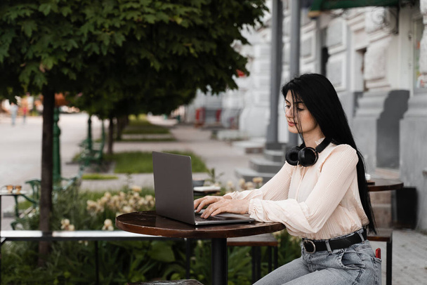 Mujer con pigmentación de la piel vitiligo en las manos que trabajan en el ordenador portátil en línea y escuchar música con auriculares al aire libre en la cafetería. Enfermedad estacional - Foto, Imagen