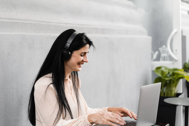 Mujer feliz con pigmentación de la piel vitiligo en las manos que trabajan en el ordenador portátil y escuchar música. Estilo de vida con enfermedad estacional de la piel - Foto, Imagen