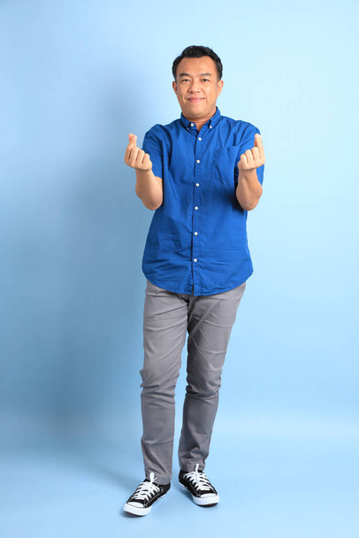 The Asian middle aged man with blue shirt standing on the blue background. - 写真・画像