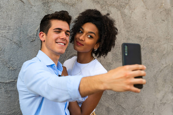 Giovane coppia romantica scattare selfie avendo abbracciando divertimento in città - razza mista giovane coppia prendere un selfie con smartphone felice coppia multietnica scattare foto coppia amorevole selfie in città - Foto, immagini