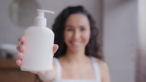 Detailní záběr mladá atraktivní šťastná žena stojící v koupelně při pohledu na kameru ukazující hydratační tělové mléko v dávkovači reklama sprcha gel péče o pleť krém propagační video z ohniska dívka - Záběry, video