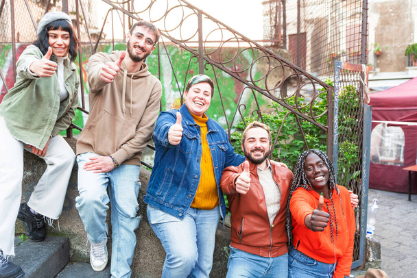 Multiethnic company spending time together, sitting outdoor - Multi-ethnic young people together for yes  portrait of smiling young diverse friends sitting on stairs outdoor together  friendship concept - Photo, Image