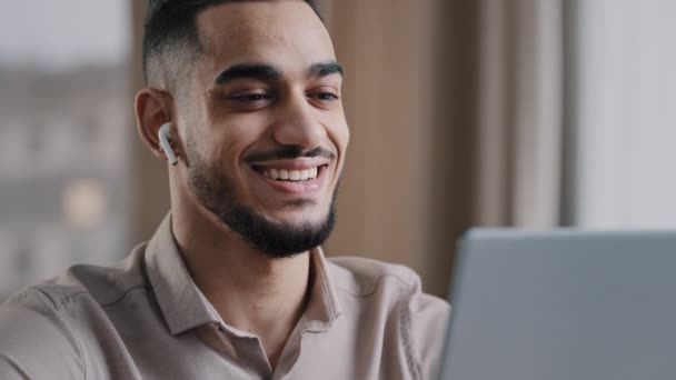 Joyeux jeune homme arabe porter des écouteurs sans fil regarder ordinateur portable relax regarder drôle vidéo comédie film sourire profiter de temps libre pause lire les bonnes nouvelles hispanique mâle beau homme d'affaires utiliser un ordinateur moderne - Séquence, vidéo