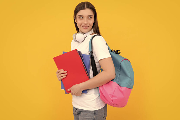Modern eğitim konsepti. Gülümseyen öğrenci defteri tutuyor. Sarı arka planda defteri tutan kız. Kitapları ve kulaklıkları olan özel bir öğretmen. Okula geri dön.. - Fotoğraf, Görsel