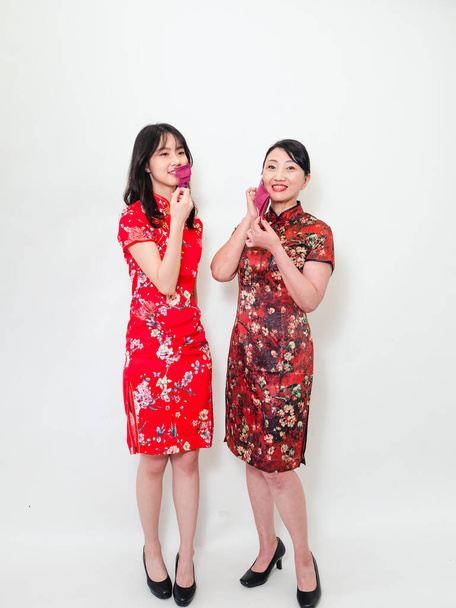 Portrait of asian women both wearing traditional cheongsam qipao dress wearing facemask during isolated on white background. - Foto, afbeelding