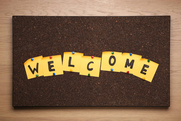 Corkboard with word Welcome made of paper notes on wooden background, top view - Foto, Imagen