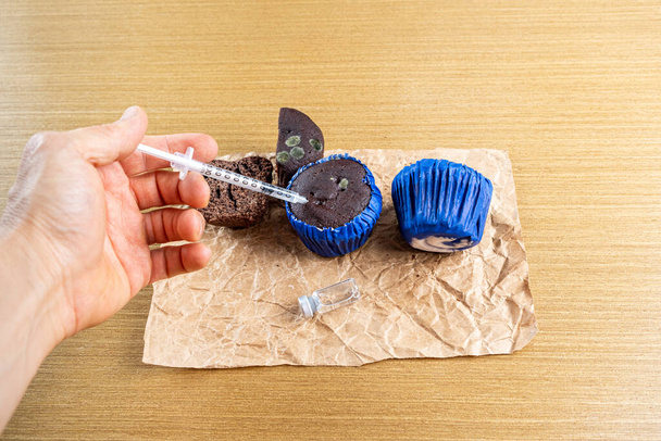 Человек со шприцем вводит инсулин в заплесневелый шоколадный кекс. - Фото, изображение
