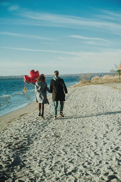 Счастливая пара с красными сердечными шариками на пляже - Фото, изображение