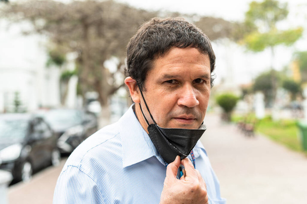 Nuori latino mies yllään lääketieteellinen naamio seisoo kaupungin - Valokuva, kuva