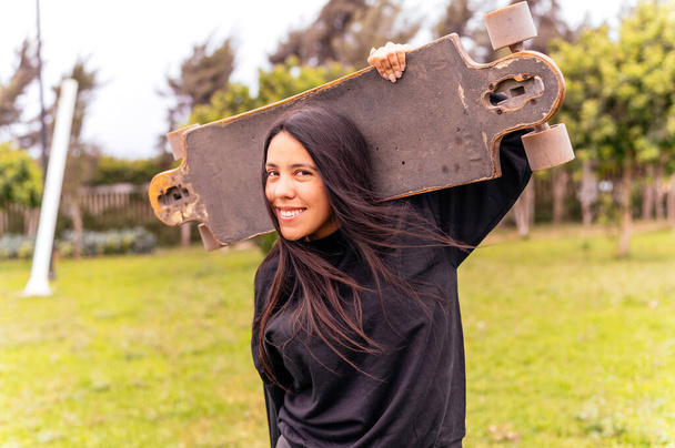 Portret van een lachende jonge vrouwelijke skateboarder die haar skateboard vasthoudt - Foto, afbeelding