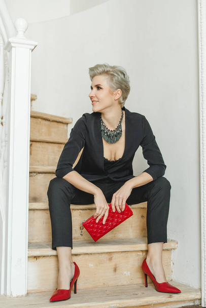 Elegante mujer modelo perfecto con traje negro de moda, zapatos rojos con tacones altos y collar de embrague de retención - Foto, imagen