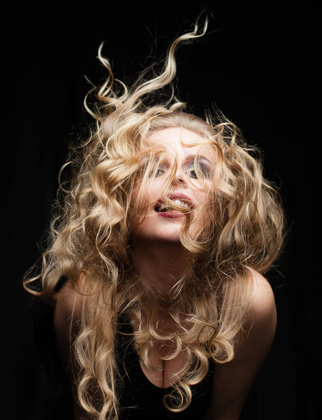 Retrato de bonita atractiva linda encantadora mujer con el pelo rubio en movimiento sobre fondo negro - Foto, Imagen