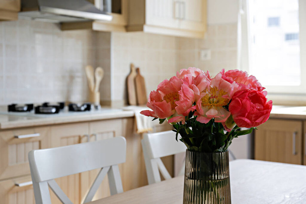 Beautiful peony flowers in glass vase on the kitchen table. Close up shot of a lush bouquet in stylish modern kitchen with small beige tile and wooden cupboard. Close up, copy space, background. - Φωτογραφία, εικόνα