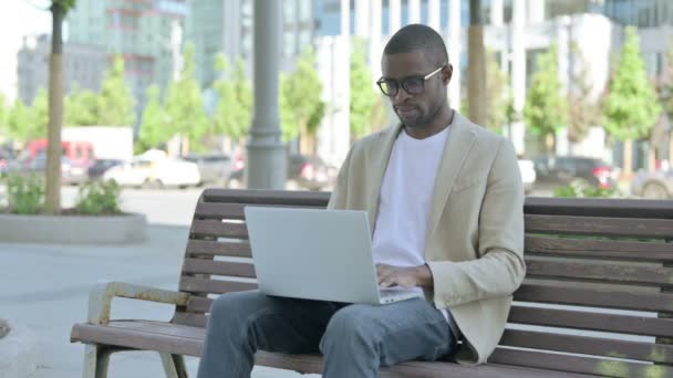 Afro-Amerikaanse man met laptop glimlachend naar de camera terwijl hij buiten op de bank zit - Video