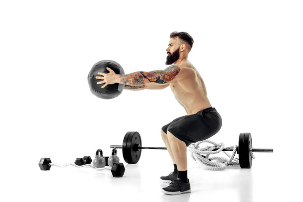 Muscular tattooed bearded male exercising fitness weights Medicine Ball in studio isolated on white background. High quality photo - Fotografie, Obrázek