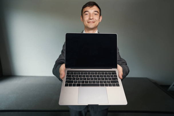 Kaukázusi férfi irodai alkalmazott nyújtja ki laptop, miközben bemutatja a kamera - Fotó, kép