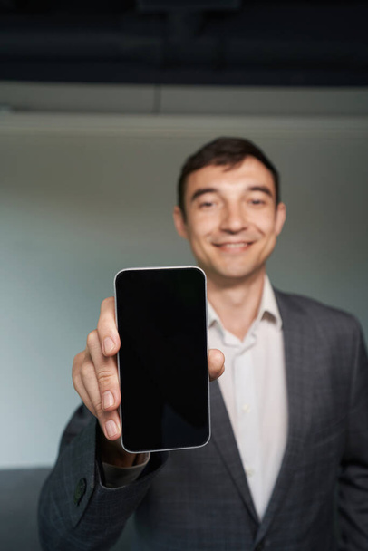 Man in formal outfit holding out mobile phone and showing it to camera - Foto, imagen
