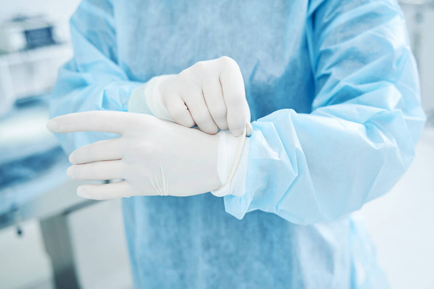 Trabajador médico con una bata quirúrgica que pone guantes de látex en las manos - Foto, imagen