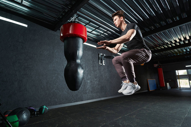 Professional athlete jumping up with knees bent during plyometric training at gym - Valokuva, kuva