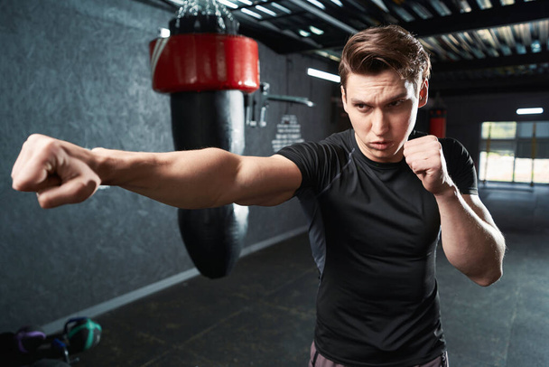 Serious focused boxer standing in fighting stance and practicing jabs during workout - Foto, Imagem