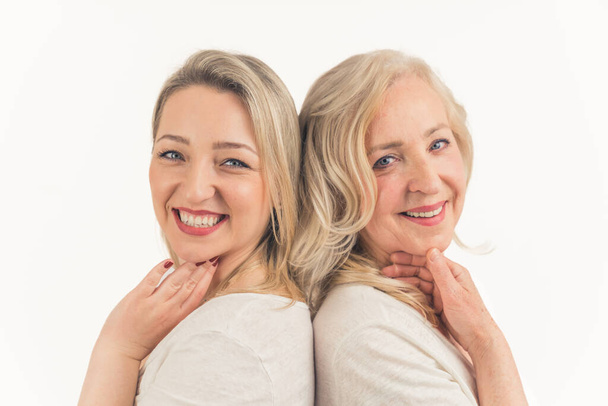 Caucasian beautiful middle-aged calm women standing back to back, touching their faces, looking at the camera. Studio shot. High quality photo - Photo, Image