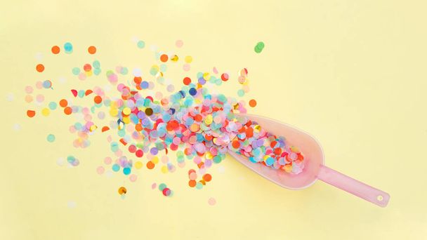 Colorful confetti in scoop on light pastel yellow background. Creative party concept. Minimalistic food composition. - Photo, image