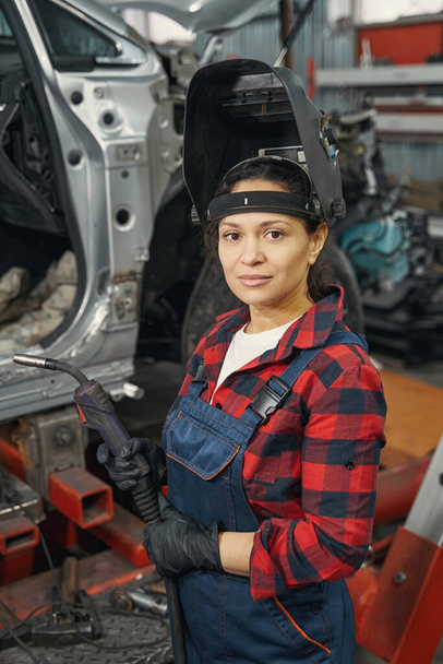 Pleased female mechanic holding welding machine while looking at camera - Fotó, kép