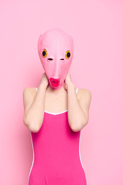 Женщина, стоящая в розовой рыбной маске на голове, провокационный сумасшедший взгляд на Хэллоуин, розовый фон в студии. Высокое качество фото - Фото, изображение