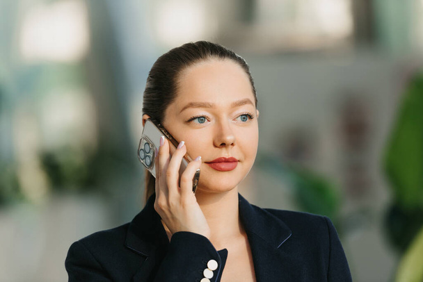 Egy közeli fotó egy női ingatlanügynökről, aki egy okostelefonon beszél. Egy kép egy nőről a modern hallban. Egy üzletasszony elhagyja az irodáját egy kortárs belső térben.. - Fotó, kép