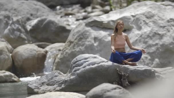 Yoga por chorro de agua - una mujer rubia sentada en la roca y meditando. Mid shot - Metraje, vídeo