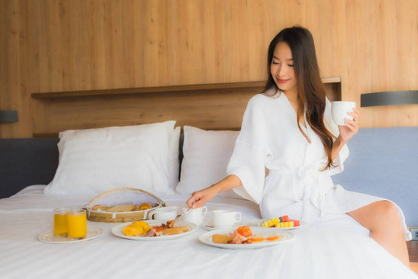 Retrato hermosa joven mujer asiática feliz disfrutar con el desayuno en la cama en el interior del dormitorio - Foto, imagen