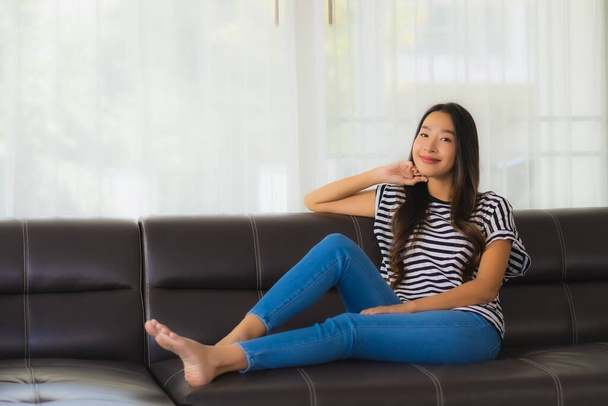 Портрет красива молода азіатка щаслива посмішка розслабляється на дивані в інтер'єрі вітальні
 - Фото, зображення