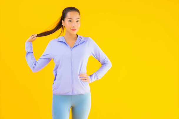 Retrato hermosa joven asiática deporte mujer con ropa deportiva listo para el ejercicio en amarillo aislado fondo
 - Foto, Imagen