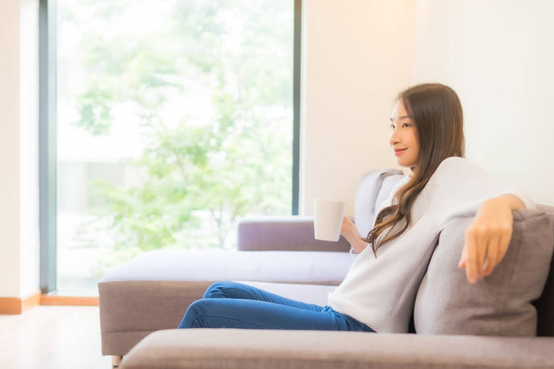 Retrato bela jovem mulher asiática com xícara de café no sofá na sala de estar interior - Foto, Imagem