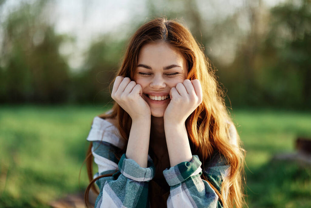 Красивая женщина на улице в зеленом парке смеется и улыбается, глядя в камеру на закат на солнце. Портрет крупного плана. Высокое качество фото - Фото, изображение