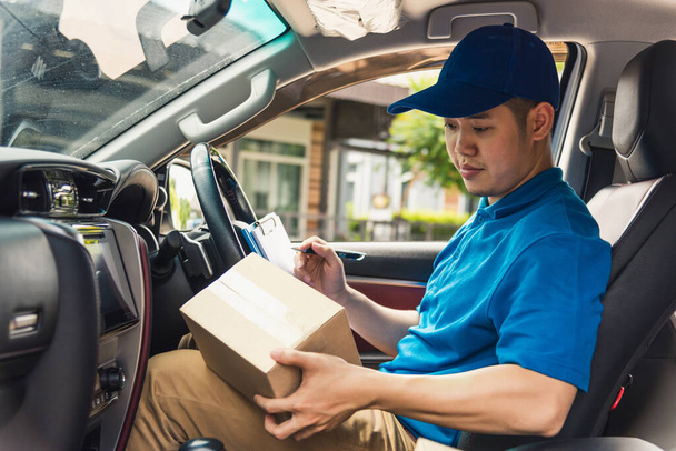 Asian young delivery man courier in uniform hold documents clipboard checking list parcel post boxes inside a car for service shipment to customer, Online shopping service concepts - Fotografie, Obrázek