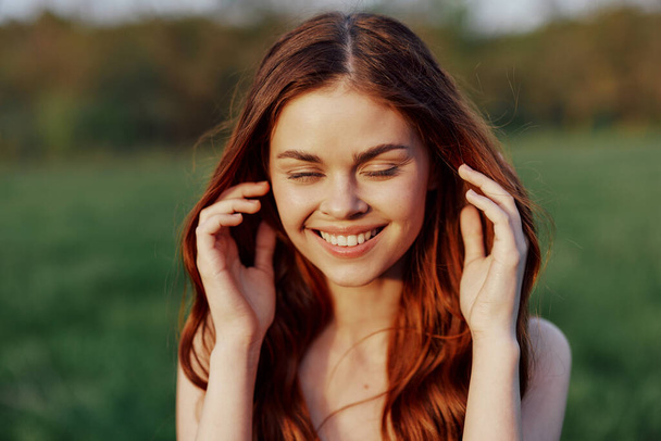 Una bella donna con lunghi capelli rossi ondulati sorride per la macchina fotografica in natura illuminata dalla luce del sole del tramonto. Il concetto di bellezza e armonia con la natura. Foto di alta qualità - Foto, immagini