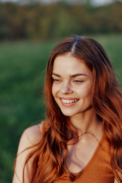 Μια όμορφη κοκκινομάλλα γυναίκα γελάει και χαμογελάει με τα δόντια της στο λαμπερό ηλιοβασίλεμα. Η έννοια της υγιούς διαβίωσης και της καλής διατροφής. Υψηλής ποιότητας φωτογραφία - Φωτογραφία, εικόνα