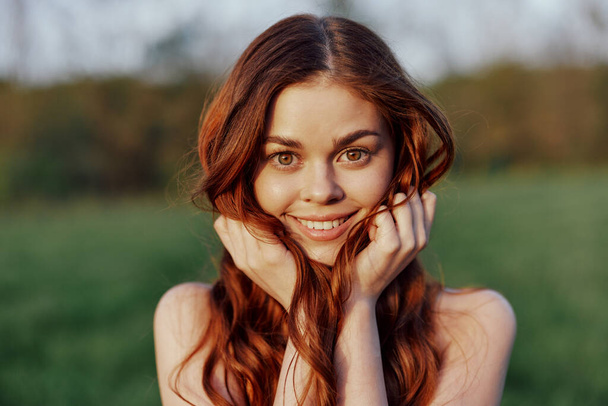 Πορτρέτο μιας νεαρής κοκκινομάλλας γυναίκας που κοιτάζει στην κάμερα και χαμογελά, κοντινό πορτραίτο μιας γυναίκας που γελάει στο φως του ήλιου που δύει. Υψηλής ποιότητας φωτογραφία - Φωτογραφία, εικόνα
