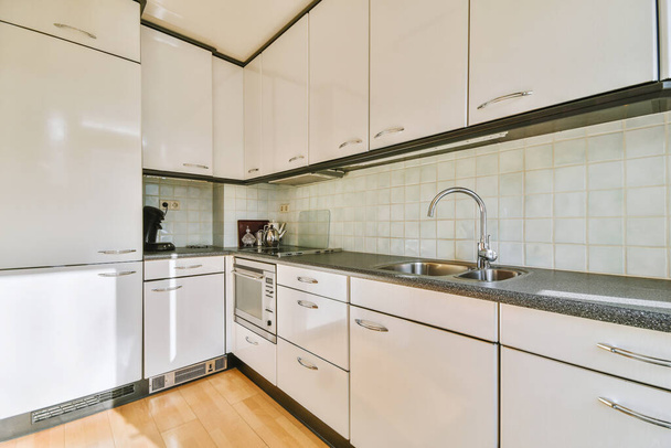Modern interior design of a corner home kitchen with white cabinets and wooden floor in a modern apartment - 写真・画像