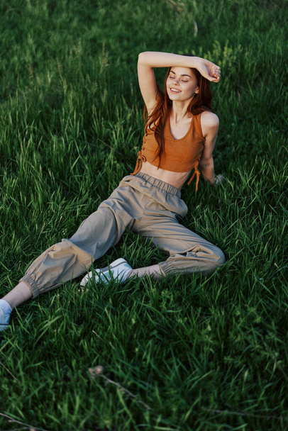 Sivrisinek ve kene olmayan bir parktaki taze yeşil çimenlerde uzanan bir kadın gün batımını izlerken dinlenmekten zevk alır. Güvenli açık hava eğlencesi kavramı. Yüksek kalite fotoğraf - Fotoğraf, Görsel