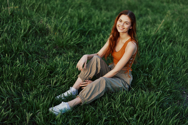Životní styl letní ženy na dovolené v parku sedí na zelené trávě a dívá se do kamery a usmívá se. Kvalitní fotografie - Fotografie, Obrázek