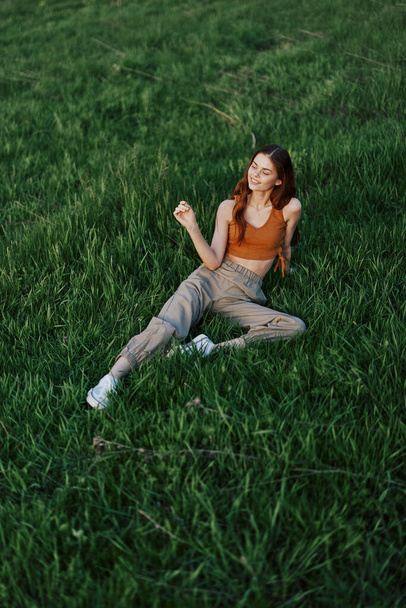 Жінка лежить на свіжій весняно-зеленій траві в парку і насолоджується розслаблюючим спостереженням за заходом сонця. Високоякісна фотографія - Фото, зображення