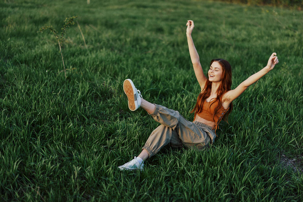 A woman lies on the green grass in the park with her legs up and having fun against the lawn, viewed from above. The concept of relaxing in nature and caring for the environment. High quality photo - Photo, Image
