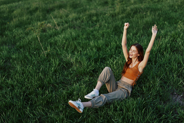 Genç bir kadın parkta bizimle birlikte çimenlerde oynuyor ve güneşin altında mutlu bir şekilde yere düşüyor. Doğada dinlenmek, bedenle uyum içinde olmak. Yüksek kalite fotoğraf - Fotoğraf, Görsel