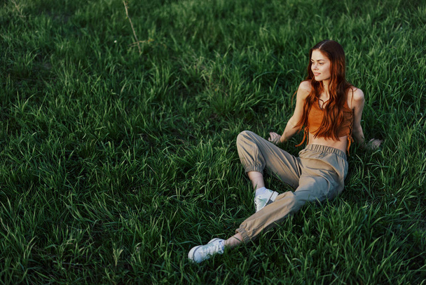 Dívka sedí na trávě v parku a má krásný výhled na letní západ slunce. Kvalitní fotografie - Fotografie, Obrázek