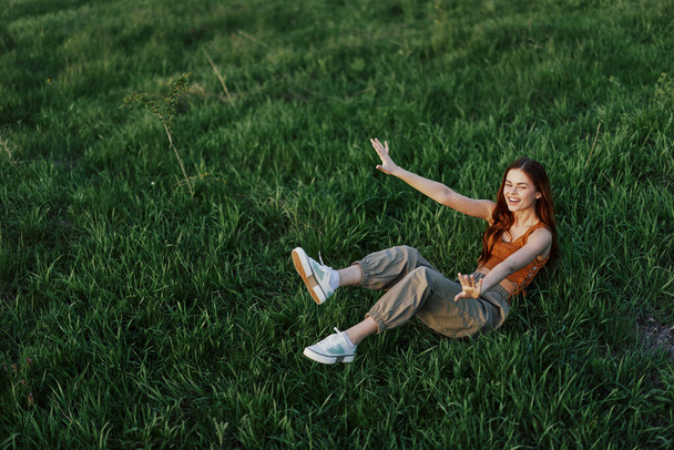 Een jonge vrouw speelt in het park met ons in het gras en valt met een glimlach op de grond in het zonlicht. Rust in de natuur, harmonie met het lichaam. Hoge kwaliteit foto - Foto, afbeelding