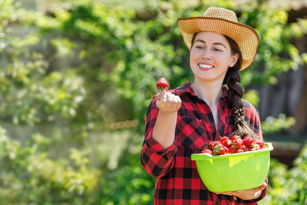 happy young woman farmer with strawberries in bowl outdoors. Harvesting, gardening and berry season concept - Valokuva, kuva