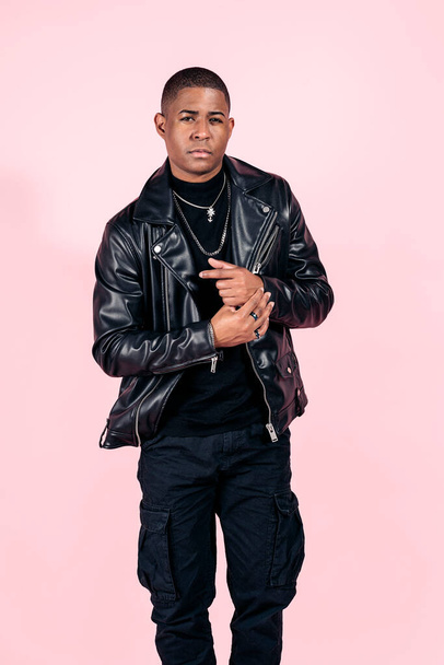 Stock photo of young black man wearing total black look posing in studio shot against pink background. - Foto, Imagen